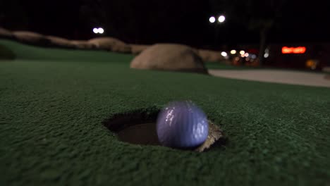 ein lila minigolfball fällt in das golfloch und springt in der tasche auf einem golfplatz