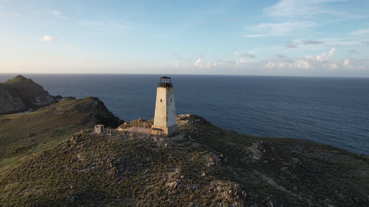faro de los rocas en la cima de una colina, rodeado de océano y naturaleza, vista aérea