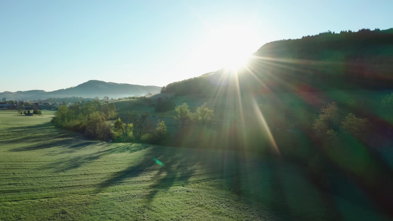 녹색과 농경지가 있는 평화로운 시골에서 아침 시간의 공중 드론 보기, 태양이 카메라, 스위스에 직접 비추고 있습니다.