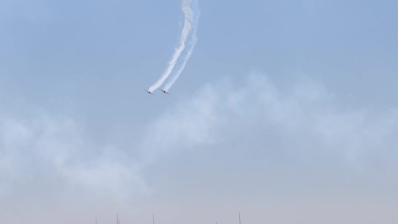 Jets create intricate smoke trails in the sky above a distant coastline, showcasing precision and skill.