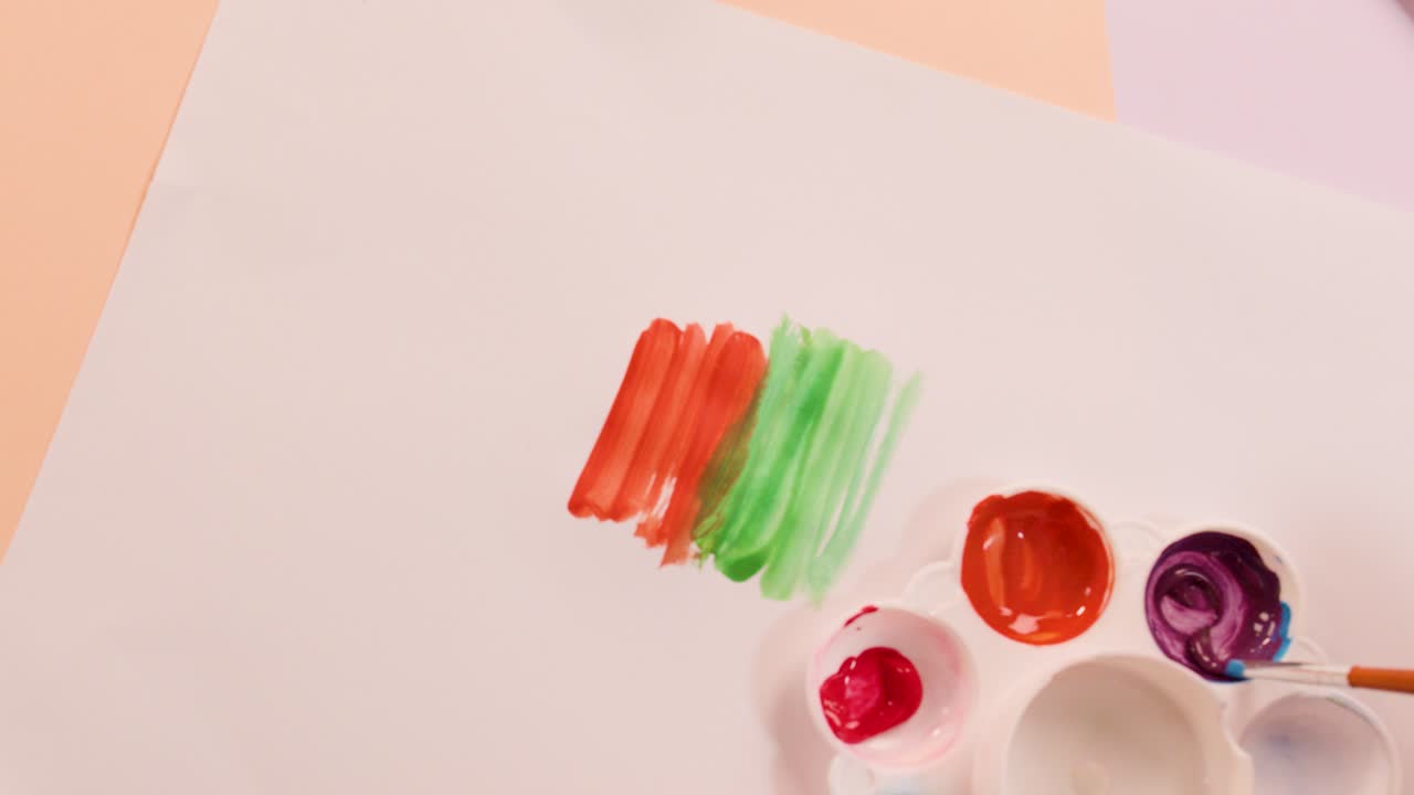 Hand mixes vibrant paints on white paper using brush, palette, overhead view, soft lighting