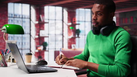 vertical video smiling black man taking notes while watching a tutorial presentation