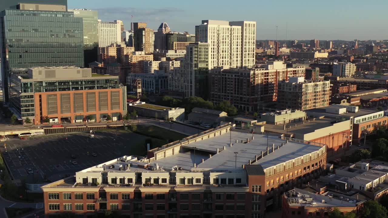 Quick aerial settle showing big buildings by harbor in Baltimore Maryland at golden hour sunrise