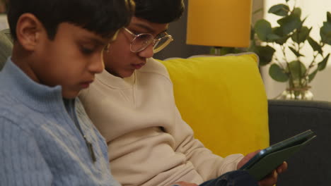 dos niños pequeños sentados en el sofá en casa jugando juegos o transmitiendo a tabletas digitales 13