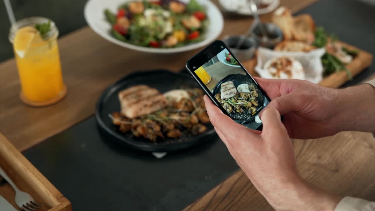 close-up of phone screen in male hands taking off food on table in restaurant