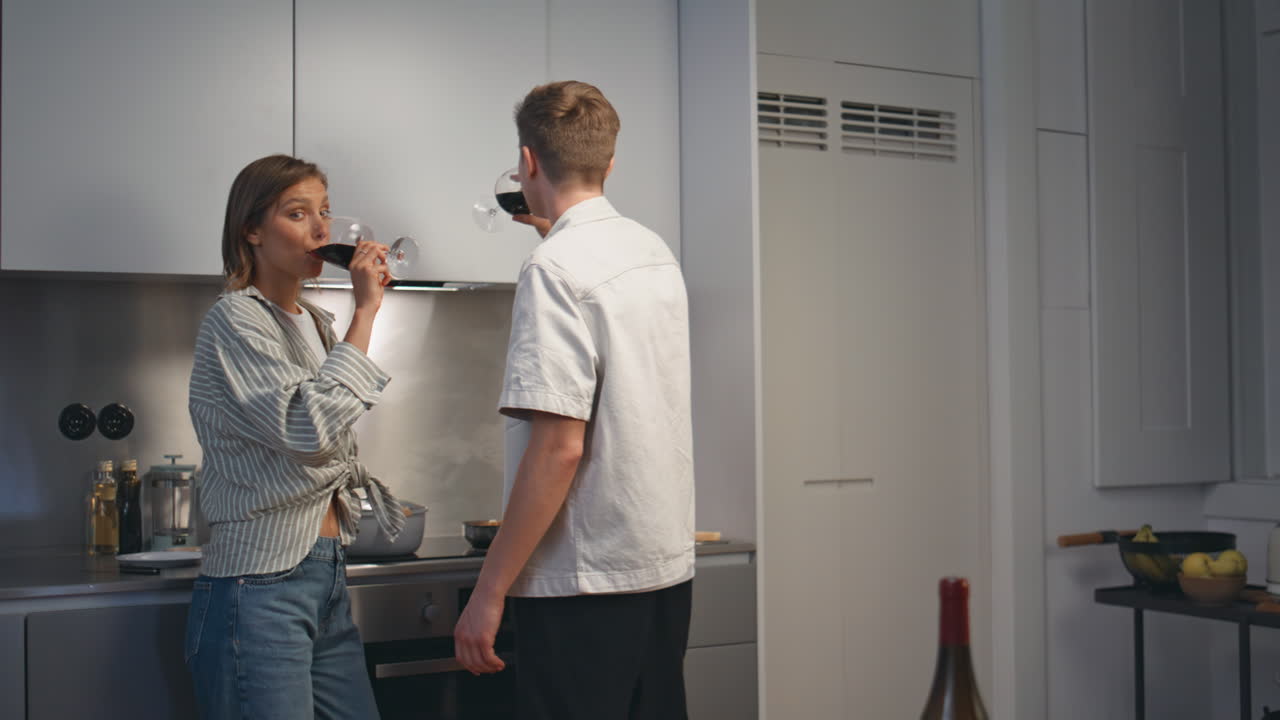 Love couple clinking goblets in modern kitchen. Smiling husband giving toast