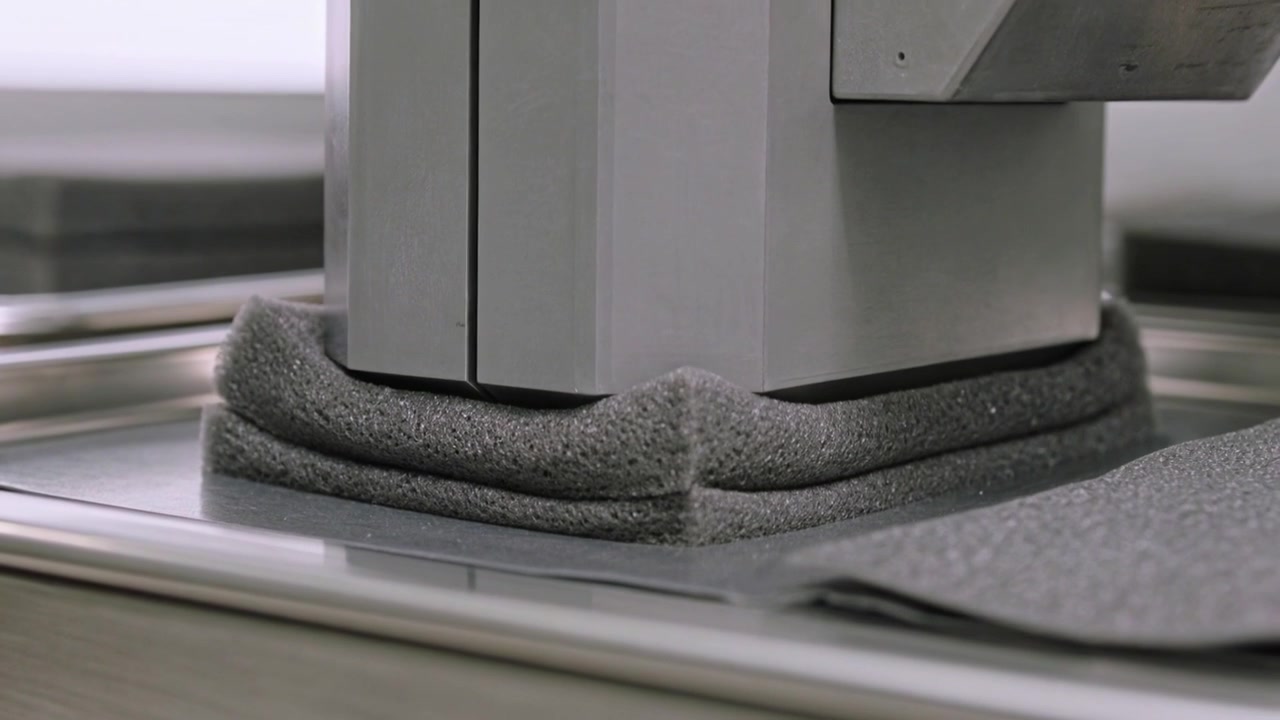 Compressing rectangular grey foam pad, square metal press lowering on steel tray for crush test