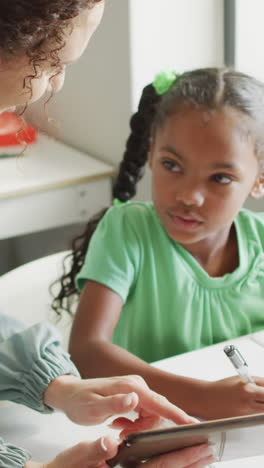 video of happy caucasian female teacher explaining lesson on tablet to african american girl