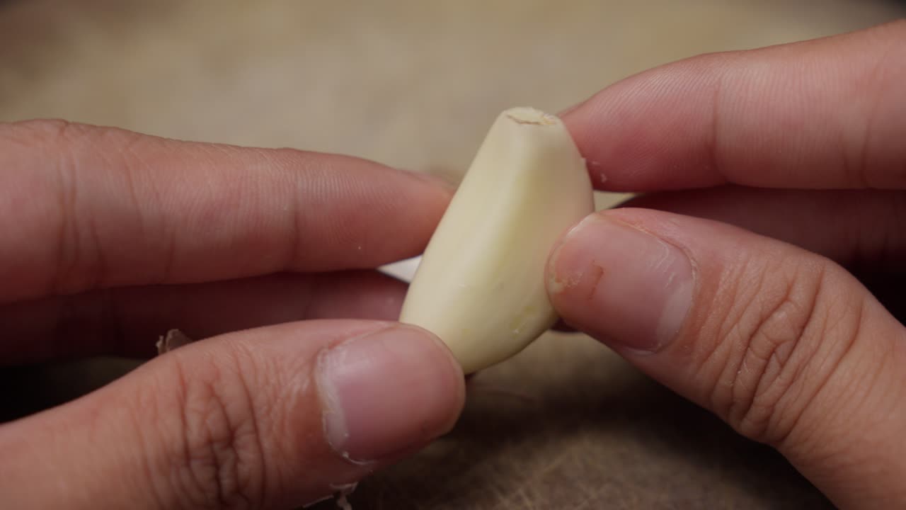 Close-up of hands peeling garlic clove for cooking preparation