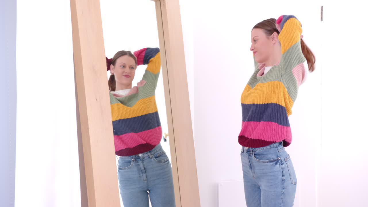 Looking in mirror, woman in colorful sweater adjusting hair, feeling relaxed