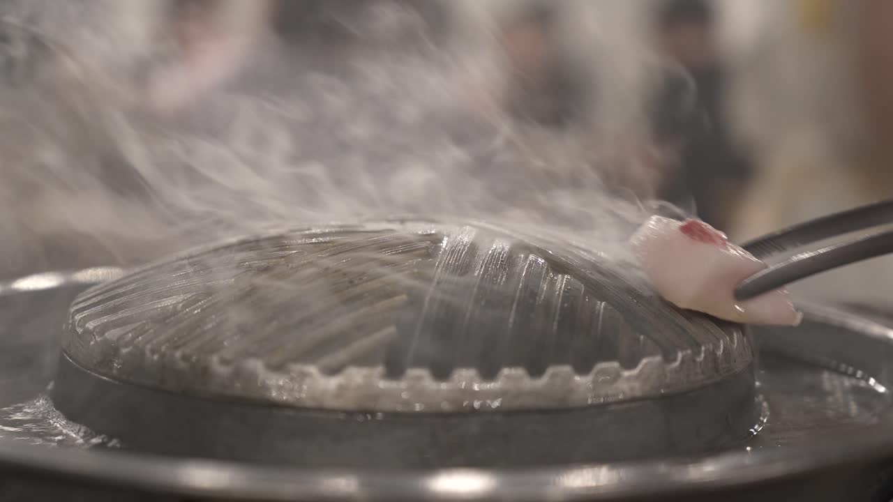 Close-up shot of raw meat being cooked on a metal hot plate in a restaurant