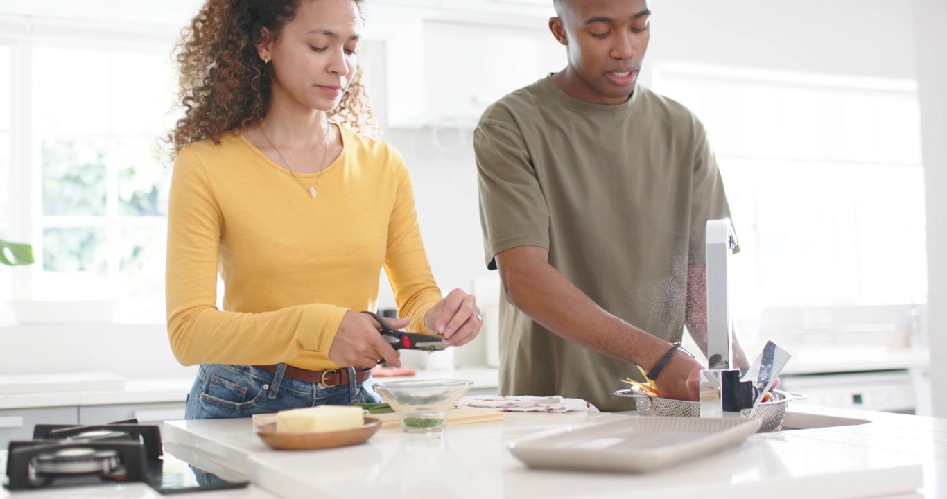 Couple making dinner on island woman cutting herbs African American man rinsing veg in colander