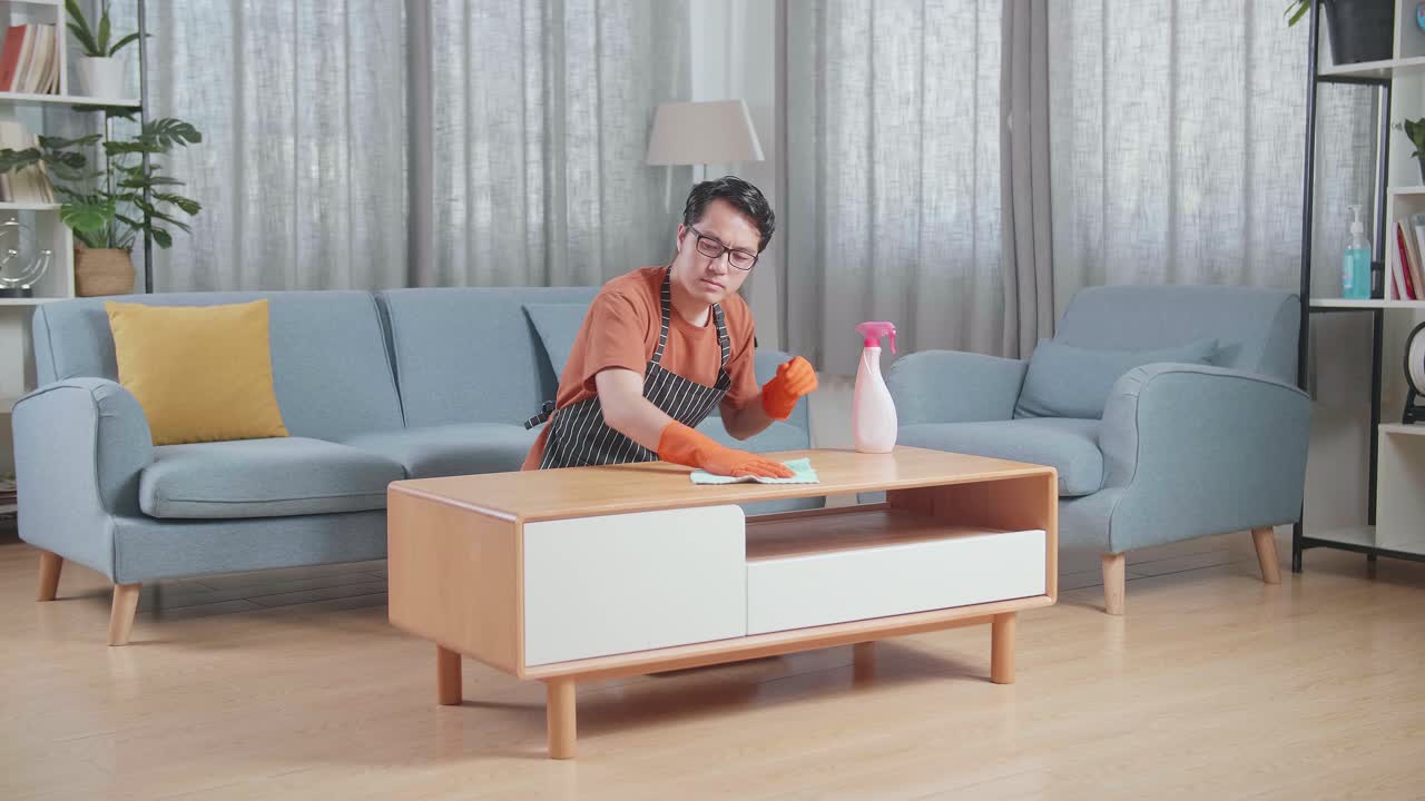 슬픈 아시아 남성 집주인이 집에서 스프레이로 테이블을 청소하고 있습니다.