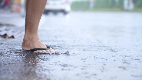 low angle shot of feet and flipflop kicking water splashing on the road side, hard raining day, flooding street, having fun enjoy playing with rain and water, close up lower body, weather rainy season