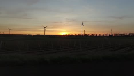 Turbinas-De-Viento-Entre-Campos-De-Cultivo-Durante-Una-Puesta-De-Sol,-Disparo-De-Drones-De-Viaje