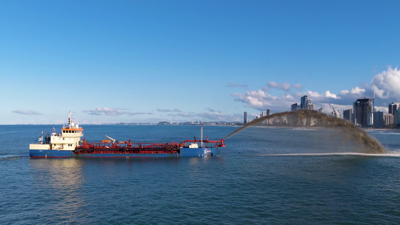A dredging ship pumps sand onto the Gold Coast shoreline under clear skies, combating erosion with urban skyline in the background