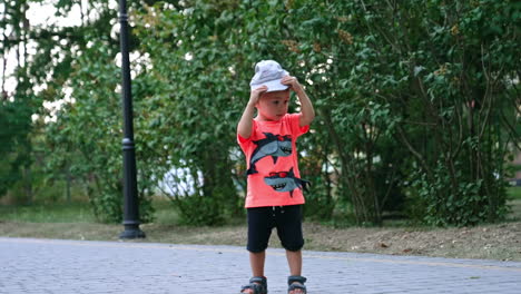 adorable toddler in t-shirt and shorts stands in the park. baby boy holding his cap.