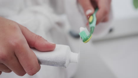 Close-up-of-biracial-woman-applying-paste-on-toothbrush-in-bathroom,-slow-motion