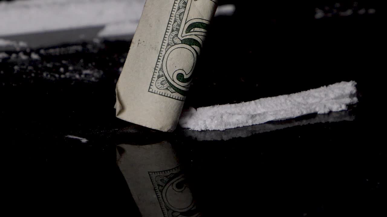 매끄러운 검정색 배경에 격리된 압연 지폐로 코카인 라인을 코로 킁킁거리다