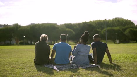 Happy-friends-sitting-on-green-lawn-and-talking