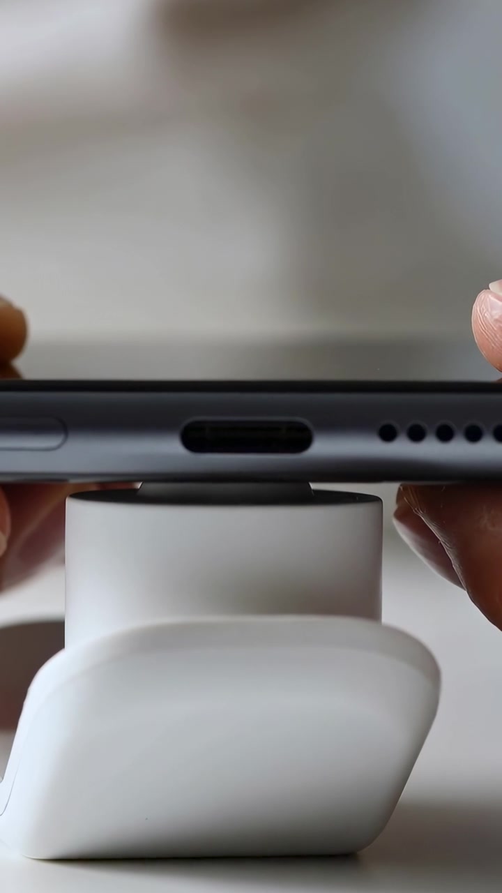Vertical video: Lowering phone, hands aligning USB-C port over charger to charge device on tabletop