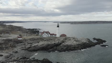 drone shot, of a lighthouse, on a rocky coastline, during a cloudy day, flying to the right.