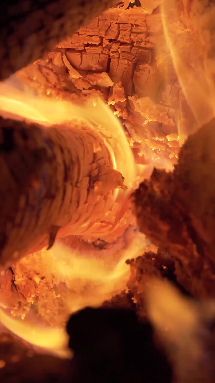 Primo piano verticale di fiamme arancioni incandescenti che tremolano tra ceppi di legno che bruciano all'interno di un accogliente falò o focolare.