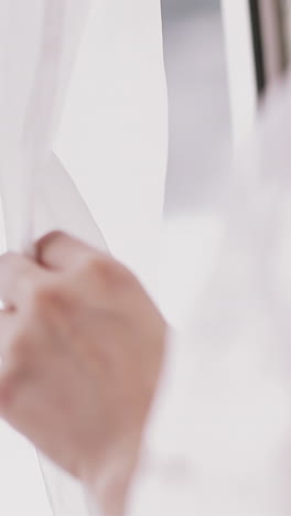 cu shot, slow motion: elegant young woman wearing stylish gentle white lacy peignoir opens window curtain in light bedroom in morning close view