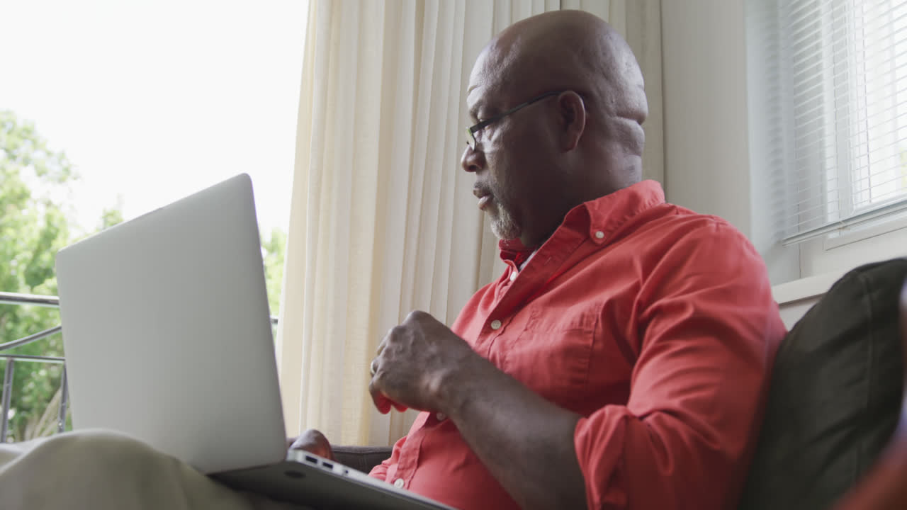 Senior african american man sitting and using laptop in living room