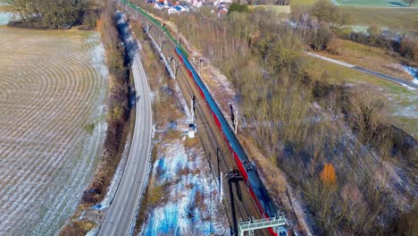 vibrant red train traversing alongside frosted fields