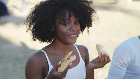 a woman looks surprised while eating a sandwich outdoors