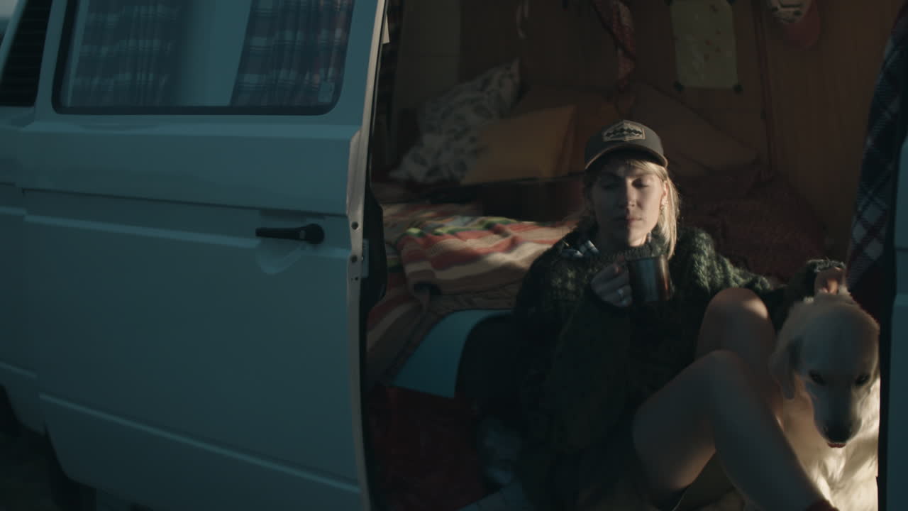 저녁 에 캠퍼 밴 에 있는 여성 관광객 이 차 를 마시고 애완견 을 키우고 있다