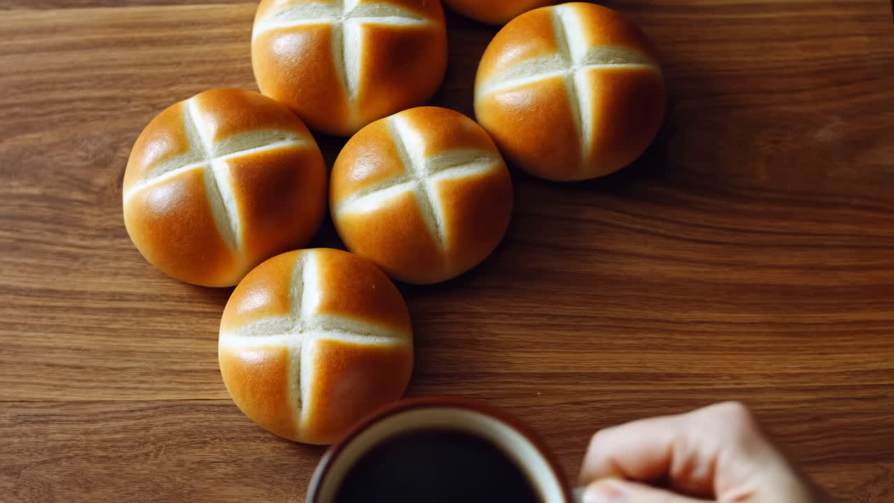 Рука берет чашку кофе рядом со свежими булочками на деревянном столе
