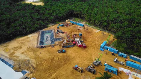 cinematic drone footage of onshore drilling rig equipment structure for oil exploration and exploitation in the middle of jungle surrounded by palm oil trees during sunset and high oil price