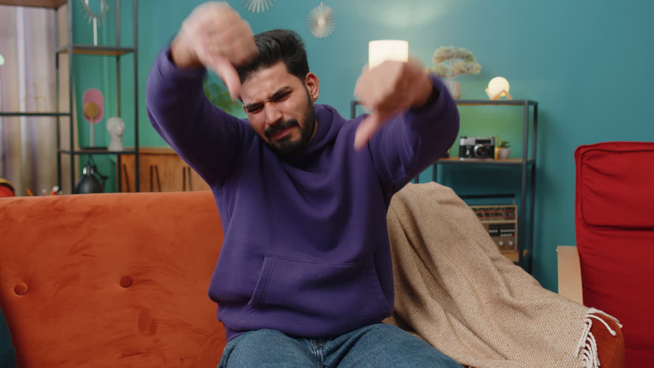 Upset indian man showing thumbs down dislike bad work disapproval dissatisfied feedback at home