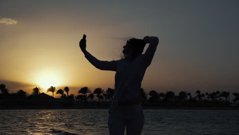 mujer atractiva tomando una selfie en el teléfono móvil en la costa al atardecer.
