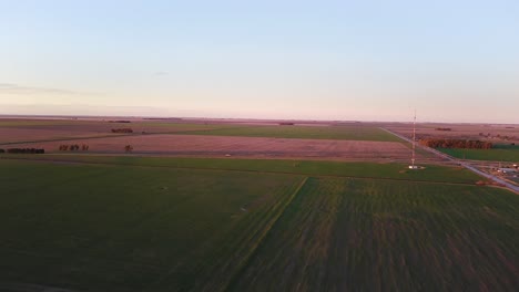 aerial view of a green rural field at sunset with a vehicle going through it on a road