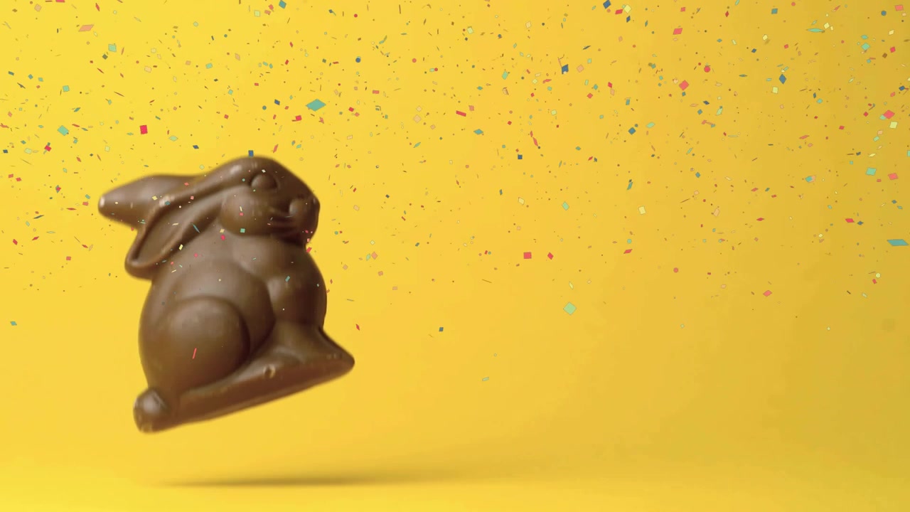 Coelho de chocolate entrando pela borda superior, girando e caindo em fundo amarelo com confetes para marketing