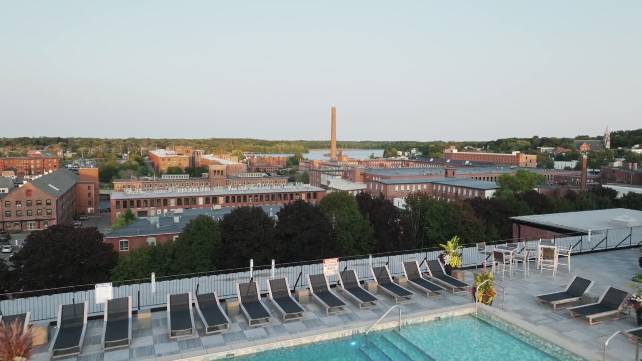 Dachpool bei Sonnenuntergang in Biddeford, Maine, mit Blick auf historische Mühlengebäude und den Saco River – urbaner Charme trifft auf entspannten Luxus.