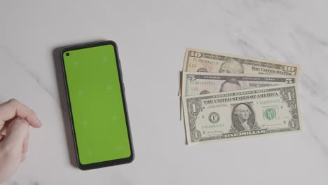 overhead currency shot of us dollar bills next to person using green screen mobile phone