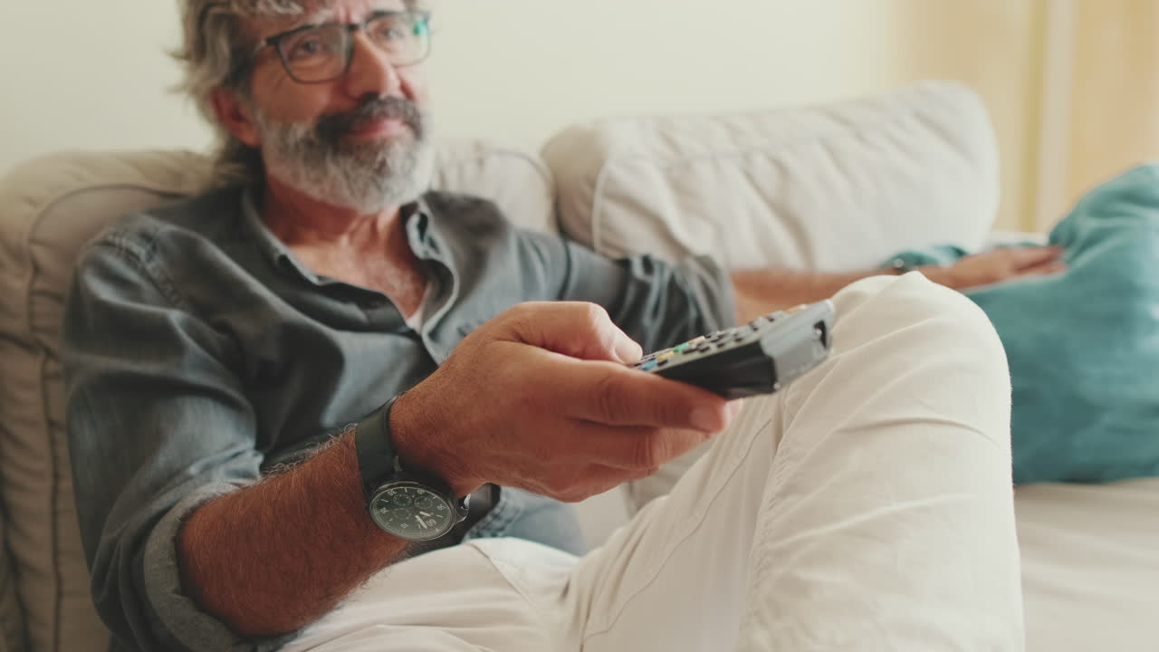 Uomo seduto su un divano con un telecomando in mano