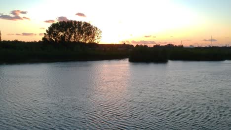 Tilt-up-drone-shot-with-orange-golden-hour-sunset-peaking-over-treeline-with-cloudscape