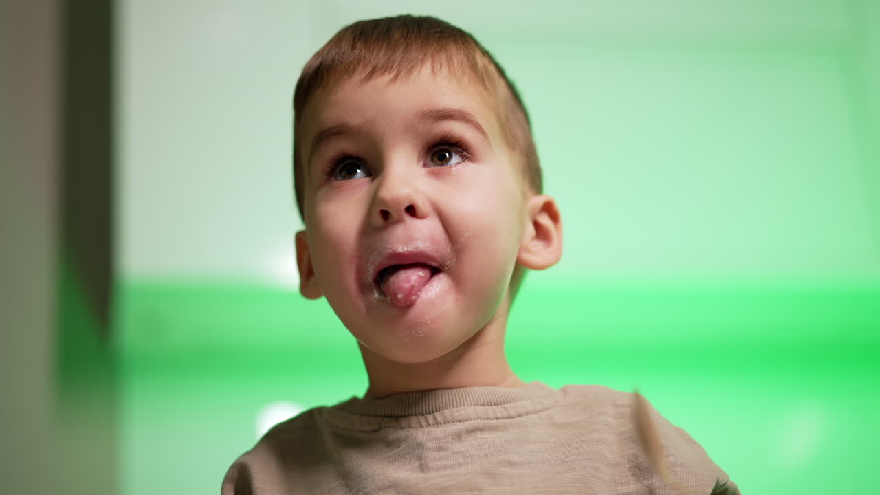 Caucasian toddler holding a spoon in his mouth. Low angle view at the baby boy eating yogurt.
