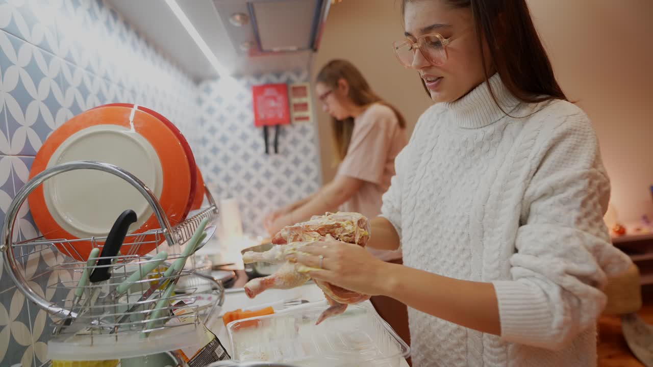 dos mujeres jóvenes preparando pollo en una cocina