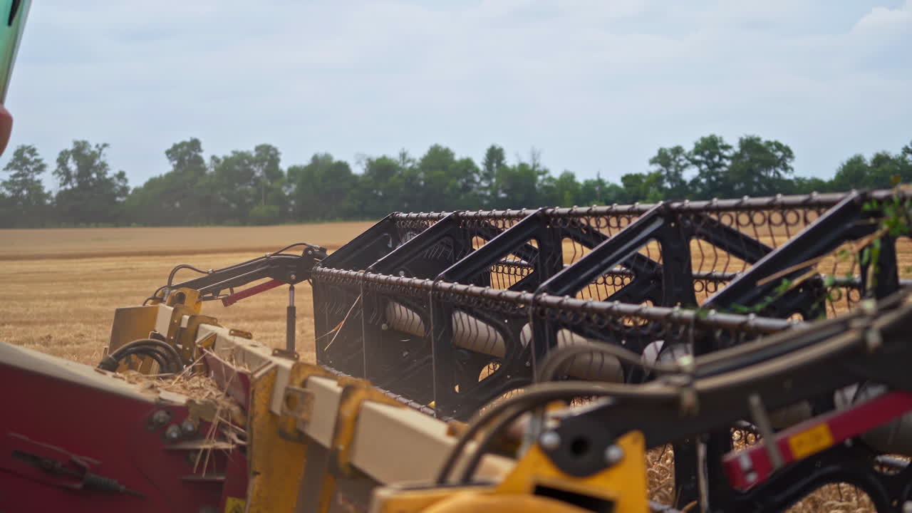 Huge mower mechanism cuts the wheat. Harvesting shears at work. Cloud of dust mixed with grains and straw coming out of massive wheels.
