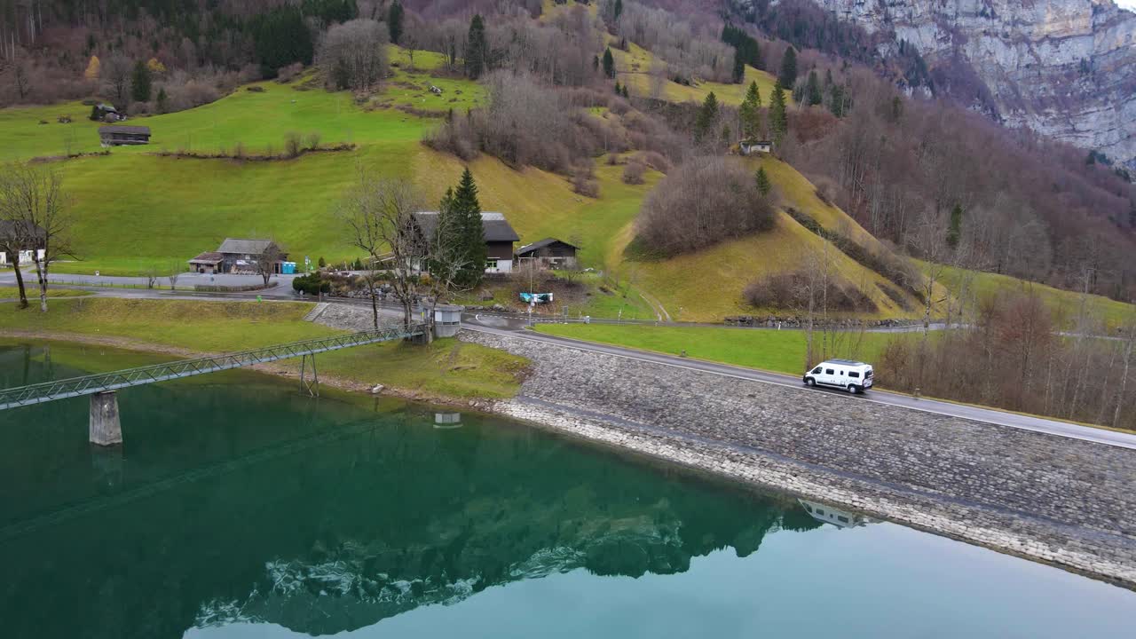 스위스 알프스의 호수 옆에 있는 댐 위를 운전하는 캠퍼 밴을 항공 추적