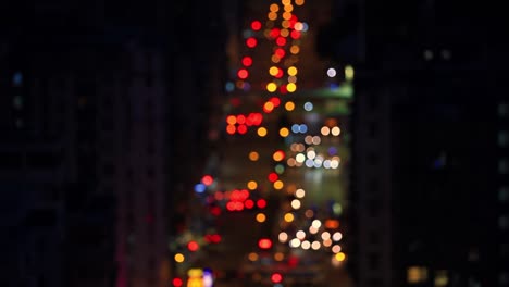 Out-of-focus-shot-of-beautifully-blurred-night-time-lapse-of-huge-street-in-between-tall-skyscrapers-with-cars-and-lights-moving-in-big-busy-city
