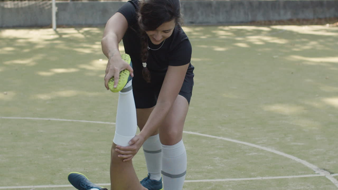 Female Football Player Doing Exercises For Flexibility With Help Of Friend On The Field