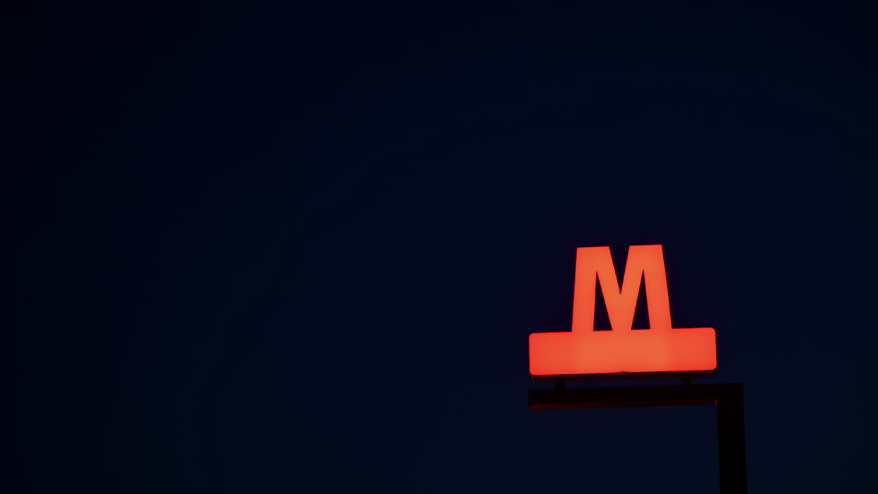 Copenahgen Metro sign with a prominent red 'M' illuminating against the dark blue sky. Denmark