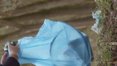 man in gloves gathers litter in bag in woods, vertical, slow motion